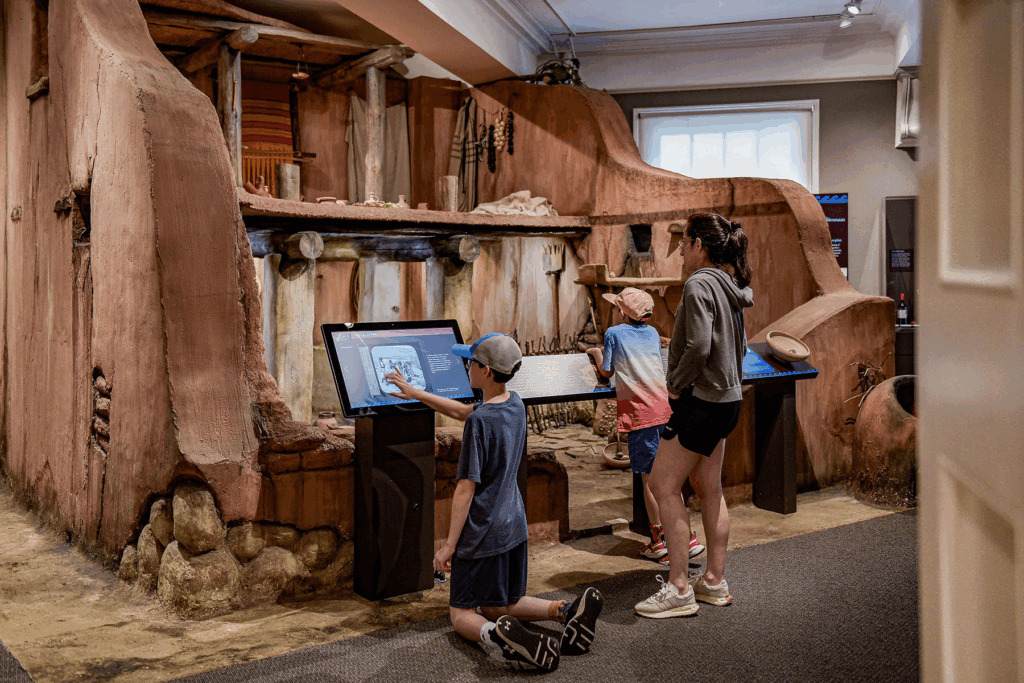 A family of tourists including two children interact with an exhibit at a Cambridge museum.