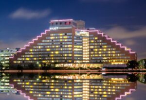 Exterior view of the Hyatt Regency Boston Cambridge, fully lit up and night and reflecting off of the water below.