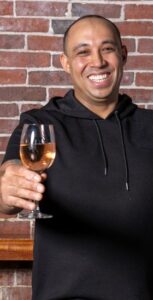 A smiling man raises a glass of rose wine against a brick backdrop in one of the best restaurants in Cambridge