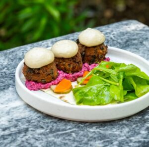 A close up of a falafel appetizer on a modern white plate. Three falafel balls with yogurt sauce sit elegantly next to a small green salad at one of the top restaurants in Cambridge