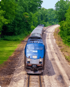 A blue MBTA commuter rail train transports passengers from Boston to Cambridge MA through a tunnel of green trees.